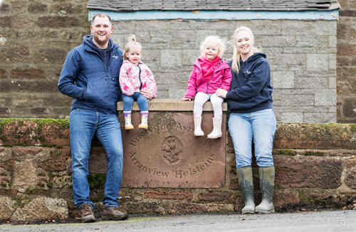 family sitting on a wall outside their farm